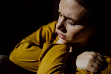 Eine Frau, die an Depressionen leidet und auf dem Boden liegt, während ihre Hände den Kopf bedecken, auf schwarzem Hintergrund. - HPIF03294