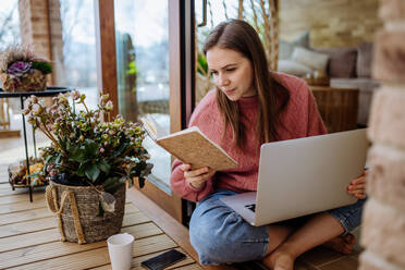 A young college student studying on laptop and using phone, when sitting on floor at home. - HPIF03302