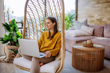 Arbeit von zu Hause aus oder online studieren, Konzept mit einer Frau, die am Laptop im Freien auf der Terrasse arbeitet und in einem Hängesessel sitzt. - HPIF03311