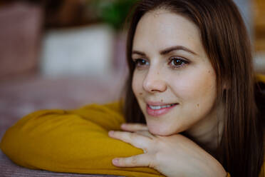 Ein Nahaufnahme-Porträt einer glücklichen jungen Frau, die lächelt und in die Kamera schaut, während sie sich zu Hause auf dem Sofa ausruht. - HPIF03312
