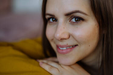 A close-up portrait of happy young woman smiling and looking at camera when restin on sofa at home. - HPIF03313