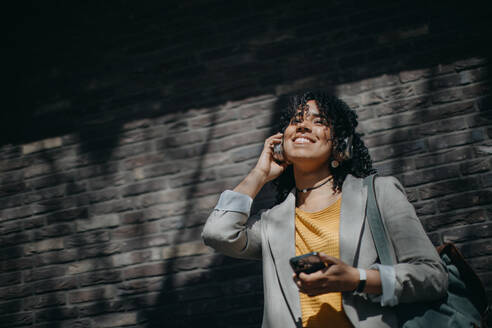 A young biracial woman wearing headphones and enjoying listening to music outdoors in street. - HPIF03335