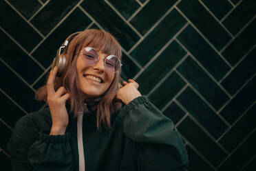 Eine junge Frau, die Kopfhörer trägt und in einem Haus Musik hört. - HPIF03345