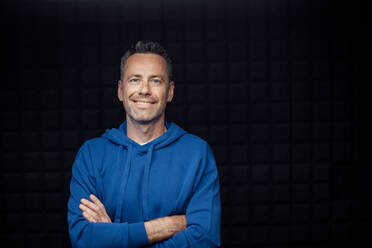 A portrait of happy mature man with arms crossed standing in studio with dark background and looking at camera. - HPIF03362