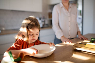 A little girl having breakfast with mother in kitchen. - HPIF03373