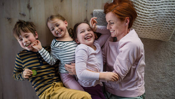 Draufsicht auf eine fröhliche Mutter mit drei kleinen Kindern, die zusammen zu Hause auf dem Boden liegen. - HPIF03378