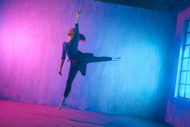 Eine moderne Tänzerin tanzt im Neonlicht und macht Gymnastikübungen im Studio, Kopierraum. - HPIF03407