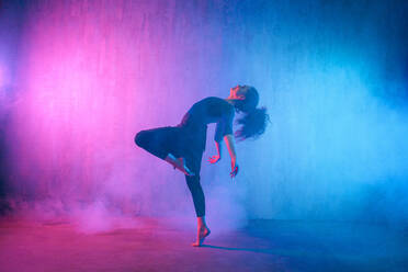 Eine moderne Tänzerin tanzt im Neonlicht und macht Gymnastikübungen im Studio, Kopierraum. - HPIF03412