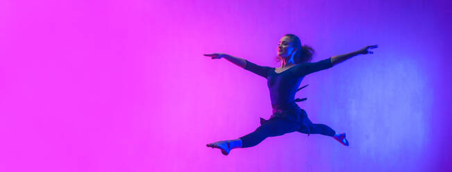 Eine moderne Tänzerin, die im Neonlicht tanzend aufspringt und gymnastische Übungen im Studio macht, breites Banner, Kopierraum. - HPIF03413