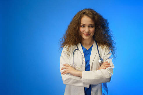 Eine Studioaufnahme einer jungen Ärztin, die vor einem blauen Hintergrund in die Kamera schaut. - HPIF03417