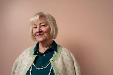 A smiling elegant elderly woman on pink color background, studio portrait - HPIF03445