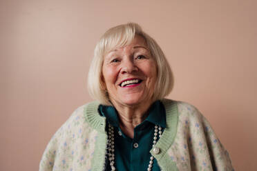 A smiling elegant elderly woman on pink color background, studio portrait - HPIF03447
