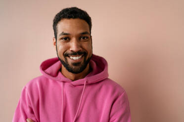 Ein Mode-Studio Porträt eines jungen afroamerikanischen Mannes in rosa Hoodie posiert über beige Hintergrund. - HPIF03457