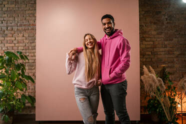 A fashion studio portrait of a happy young blonde woman in hoodie posing over pink background. - HPIF03466