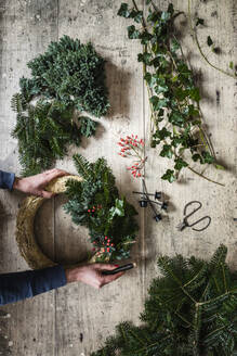 Hands of woman preparing Christmas wreath made of spruce, juniper, ivy, and rose hips - EVGF04182