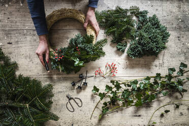 Hands of woman preparing Christmas wreath made of spruce, juniper, ivy, and rose hips - EVGF04190