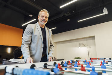 Smiling businessman playing foosball in office - VPIF07710