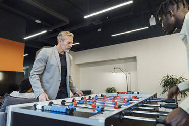 Mature businessman playing foosball with young colleague in office - VPIF07711