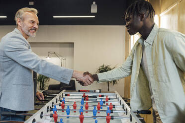 Happy businessman shaking hands with young colleague at office - VPIF07712