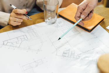 Hand of businessman pointing with pen on blueprint by colleague at table - VPIF07735