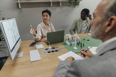 Businesswoman explaining over computer to colleagues at table in office - VPIF07756