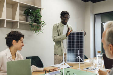 Young businessman discussing over solar panel with colleagues in office - VPIF07759