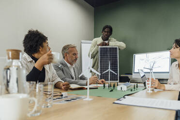 Businessman discussing with colleagues over solar panel in office - VPIF07762