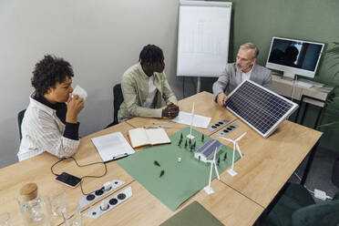 Mature businessman with colleagues discussing on solar panel at table in office - VPIF07775