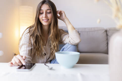 Lächelnde Frau mit Smartphone im Wohnzimmer zu Hause - JPTF01166