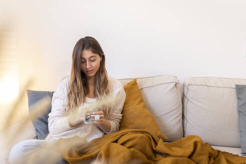 Junge Frau sitzt mit Teetasse auf dem Sofa zu Hause - JPTF01168