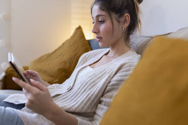 Smiling woman using tablet PC on sofa at home - JPTF01169