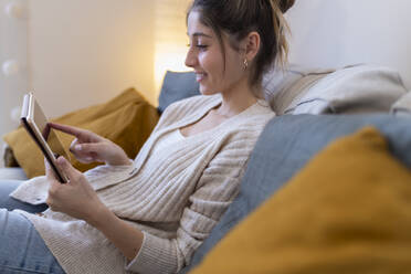 Happy young woman using tablet computer on sofa at home - JPTF01170
