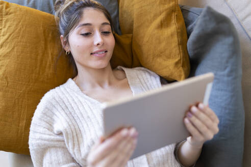Lächelnde junge Frau, die sich entspannt und einen Tablet-PC zu Hause benutzt - JPTF01175