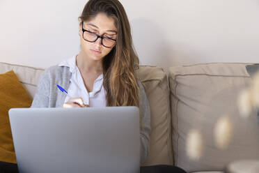 Junge Frau mit Brille studiert zu Hause am Laptop - JPTF01182