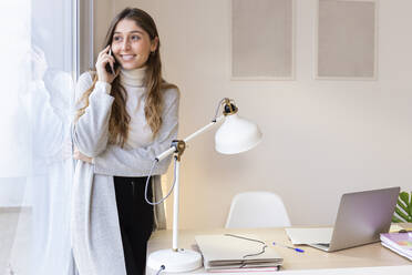 Happy young woman talking on mobile phone at home - JPTF01189