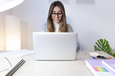 Glückliche junge Frau studiert am Laptop am Schreibtisch - JPTF01191