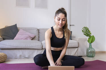 Young woman using tablet PC sitting on mat at home - JPTF01194