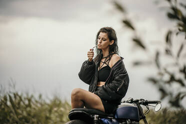 Frau zündet Zigarette mit Feuerzeug auf Motorrad an - MJRF00812