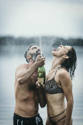 Fröhliches Paar beim Feiern mit Champagner im See - MJRF00826