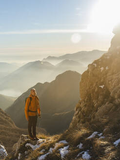 Älterer Wanderer steht auf einem Felsen vor einem Gebirge - MCVF01026