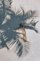 Aerial view of woman lying under tree shadow on sand - KNTF06855