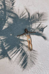 Luftaufnahme einer Frau, die im Schatten eines Baumes auf Sand liegt - KNTF06855