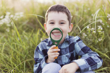 Happy boy with magnifying glass in front of plants - ONAF00319