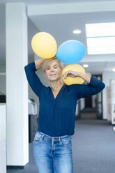 Geschäftsfrau mit geschlossenen Augen hält Luftballons am Arbeitsplatz - JOSEF15220