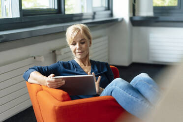 Businesswoman using tablet PC on armchair at office - JOSEF15228