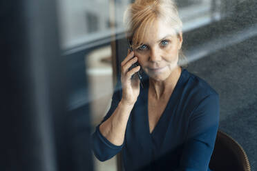 Reife Geschäftsfrau, die in einer schalldichten Kabine im Büro mit einem Mobiltelefon spricht - JOSEF15231