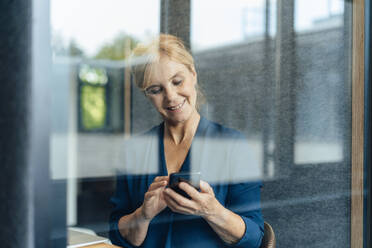 Lächelnde Geschäftsfrau, die ein Smartphone in einer schalldichten Kabine im Büro benutzt - JOSEF15243