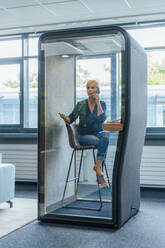 Businesswoman talking on mobile phone in soundproof cabin at office - JOSEF15245