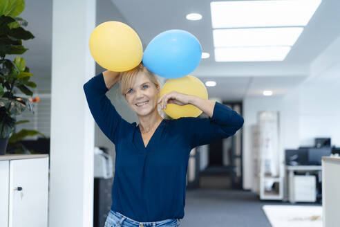 Glückliche Geschäftsfrau mit Luftballons im Büro - JOSEF15248