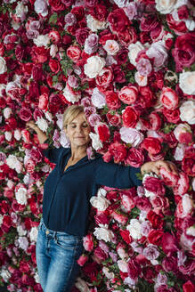 Businesswoman with eyes closed leaning on flower wall - JOSEF15266